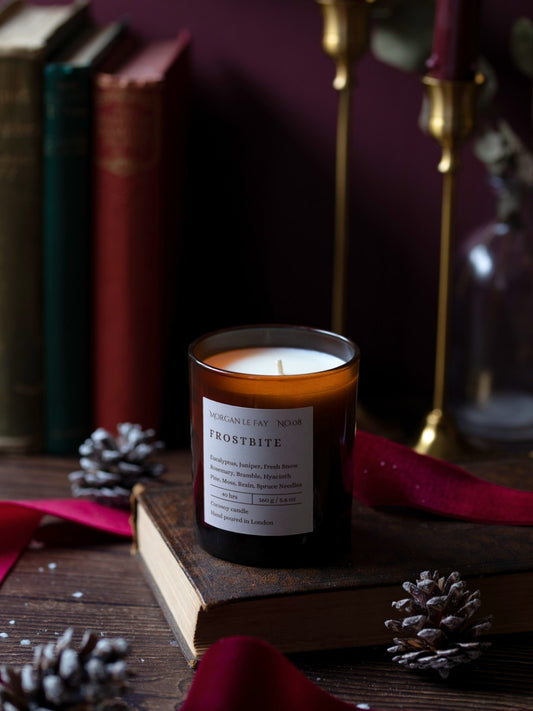 Candle labeled 'Frostbite' on a wooden surface with books and decorative elements.