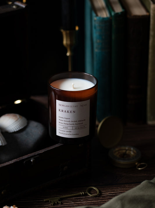 Candle labeled 'Kraken' on a dark background with books and decorative items.