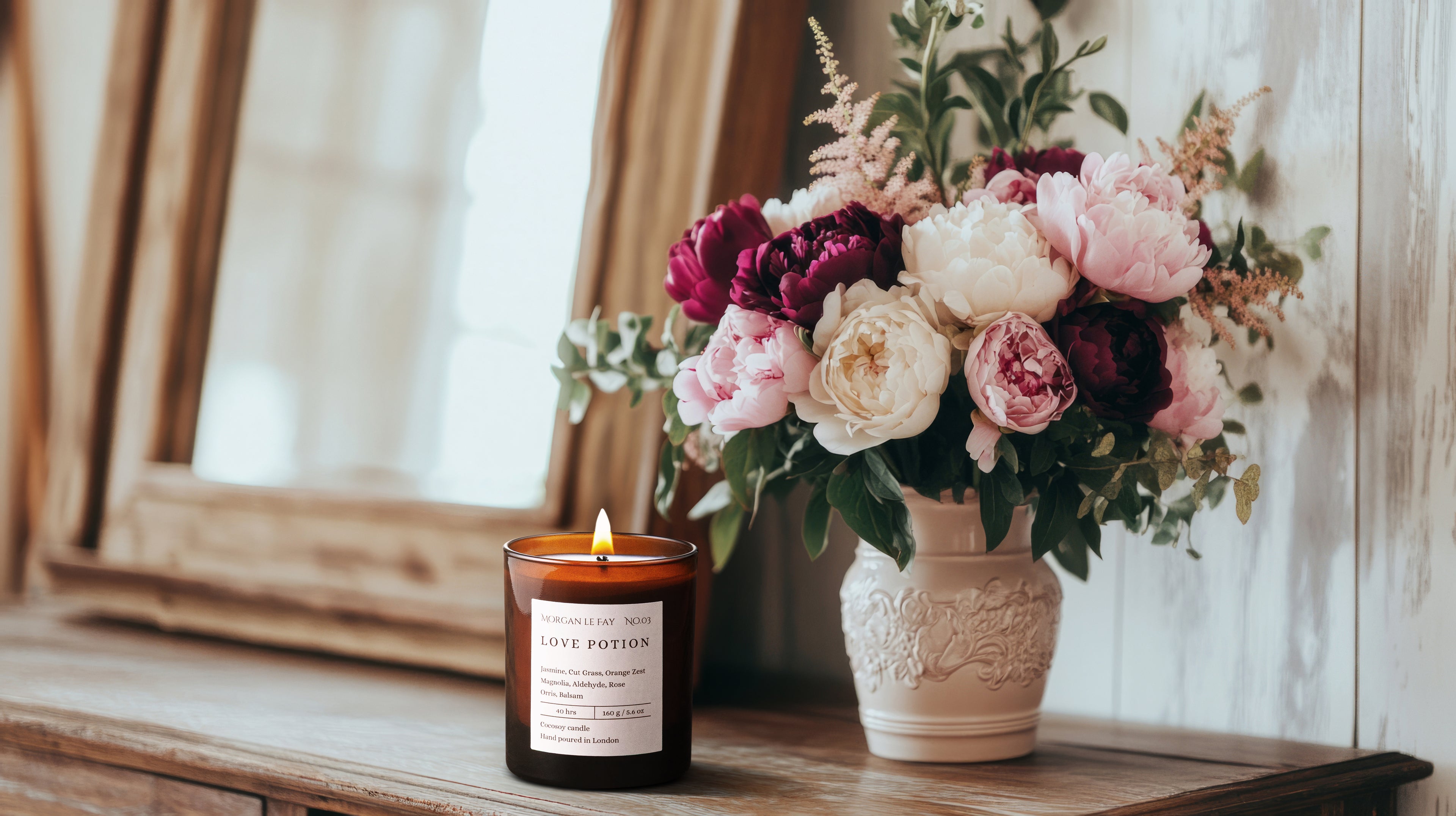 Candle and floral arrangement on a wooden surface with a mirror in the background