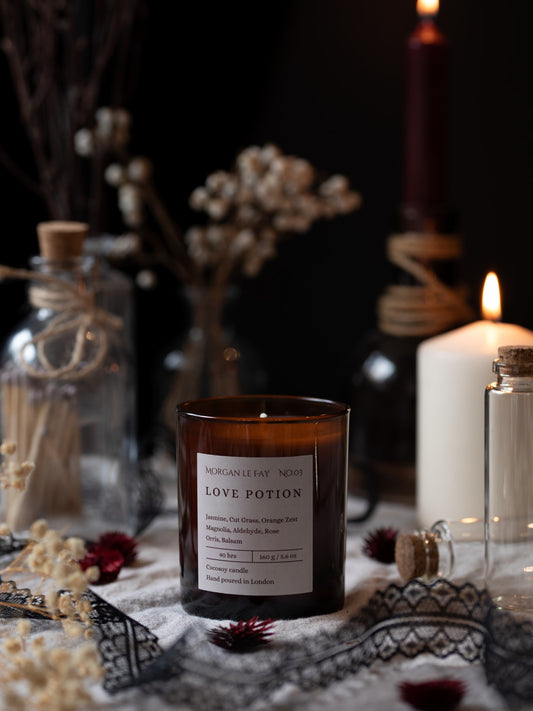 Candle labeled 'Love Potion' on a decorative table with candles and flowers.