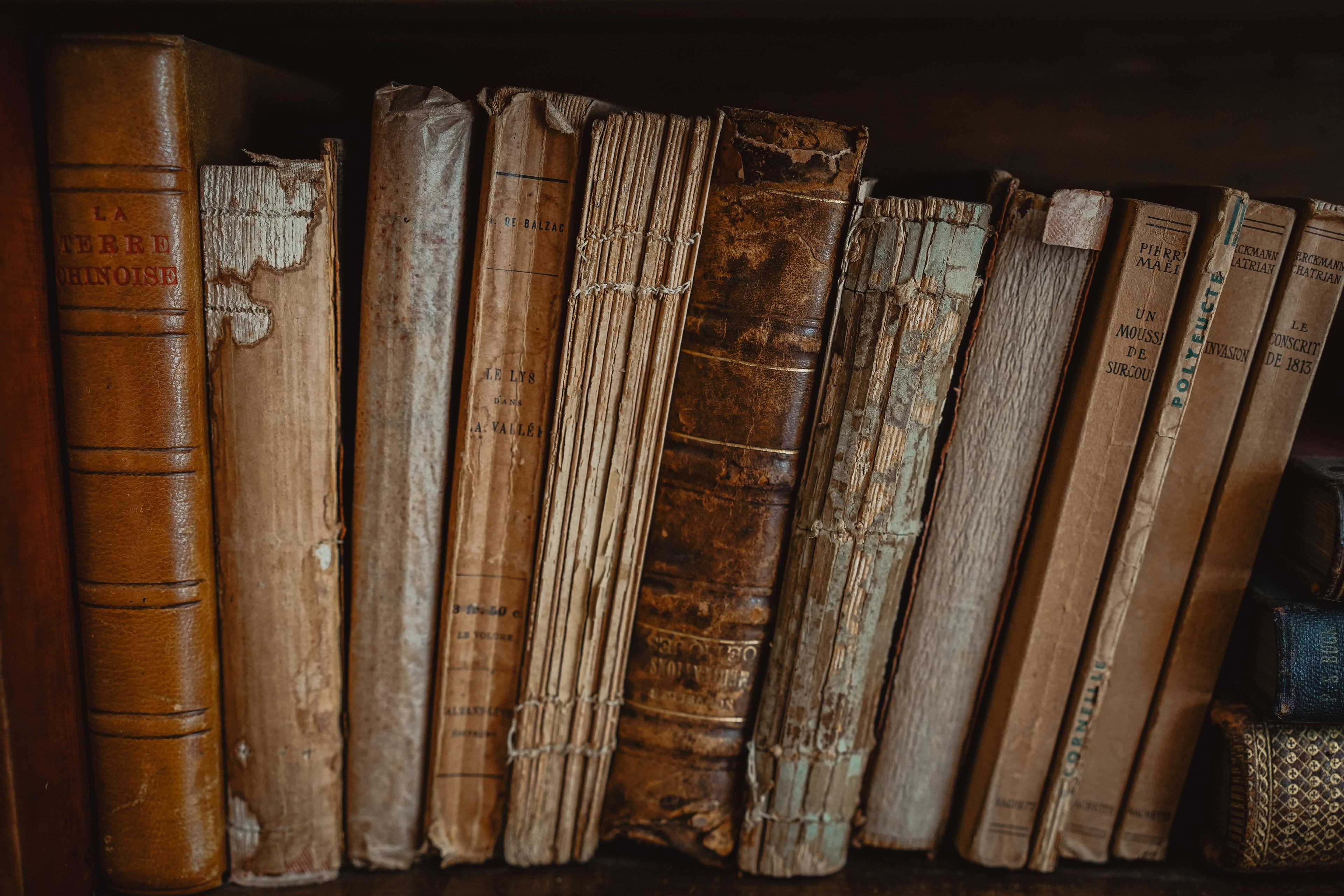Row of old, worn books on a shelf with a dark background