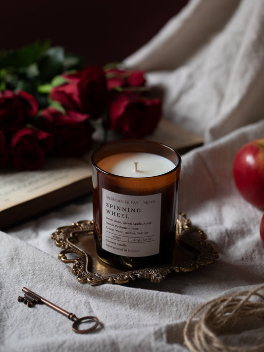 Candle in a glass holder with a label, surrounded by red roses and a key on a textured surface.