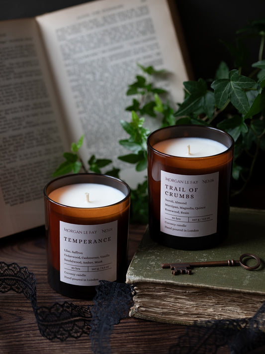 Two candles with labels on a surface with books and a key in the background