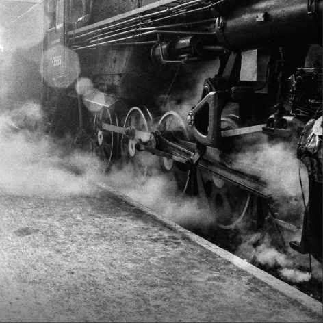 Black and white close-up of the wheel mechanism of a steam locomotive in motion.