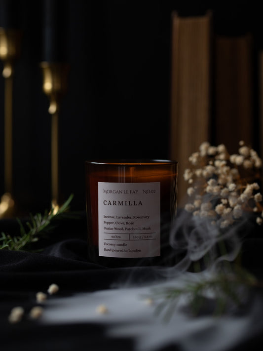 Candle with a label titled 'Carmilla' in a dark setting with decorative elements.