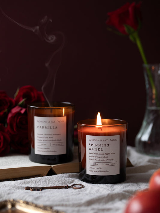 Two candles with labels on a dark background with flowers and a key.