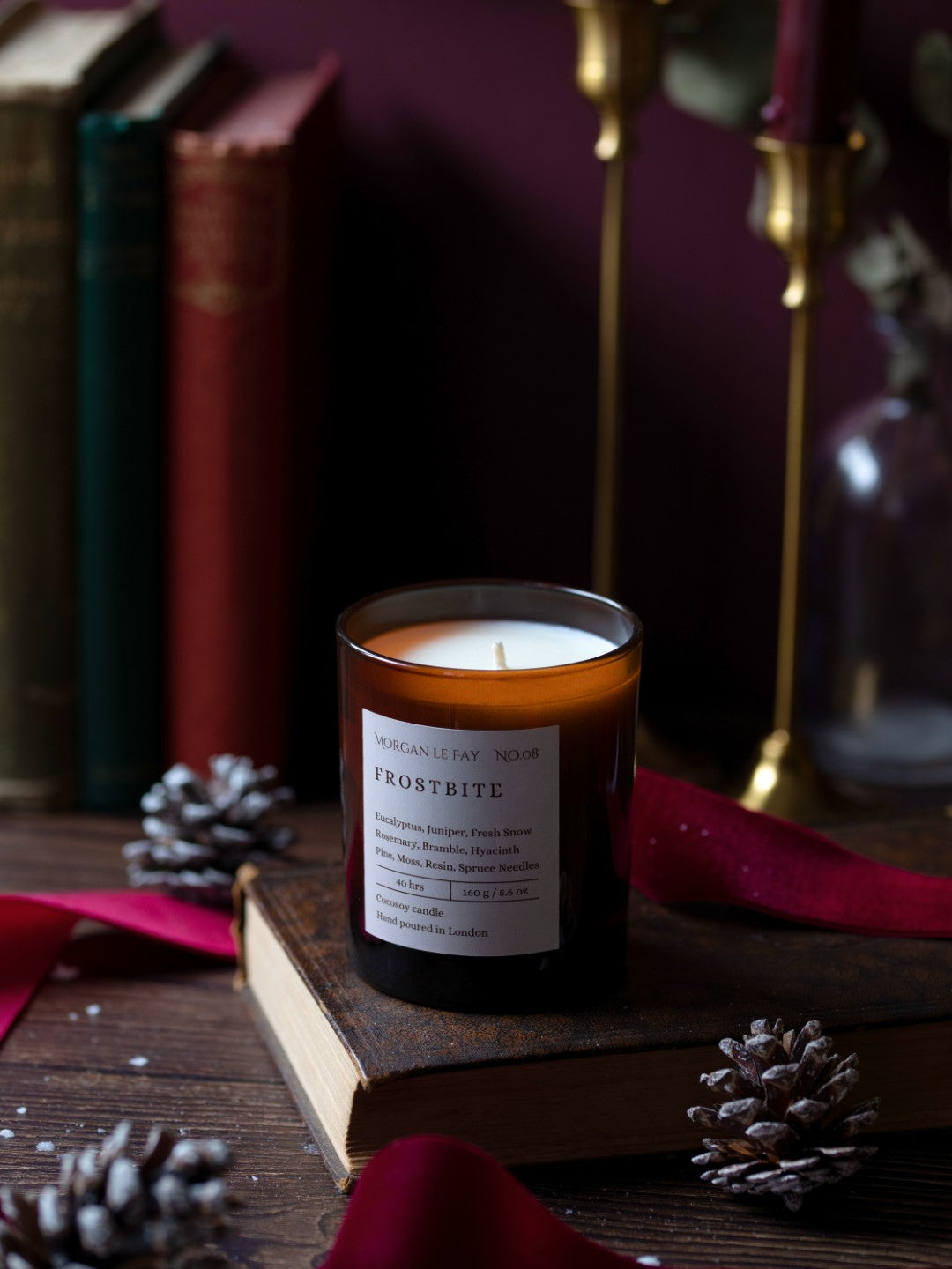 Candle labeled 'Frostbite' on a wooden surface with books and decorative elements.