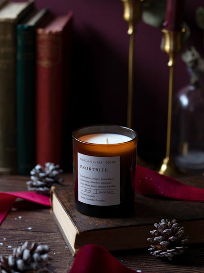 Candle labeled 'Frostbite' on a wooden surface with books and decorative elements.