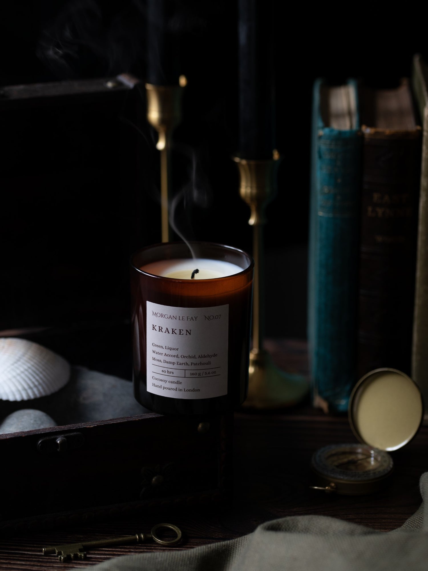 Candle labeled 'Kraken' on a dark surface with books and shells in the background