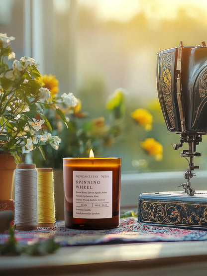 Candle labeled 'Spinning Wheel' next to a vintage spinning wheel with flowers in the background