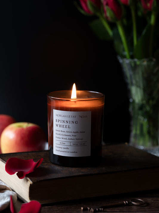 Candle labeled 'Spinning Wheel' on a book with apples and flowers in the background