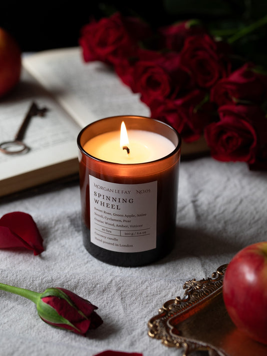 Candle labeled 'Spinning Wheel' with red roses and an apple on a textured surface