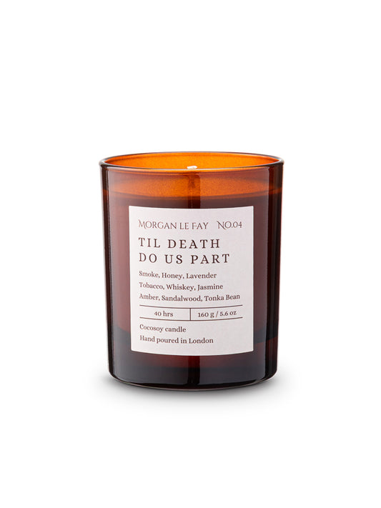 Candle with an amber transparent glass jar and a label that says 'til death do us part' on a white background