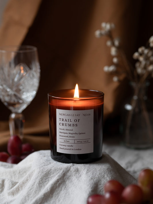 Candle with a label on a surface with grapes and a glass in the background