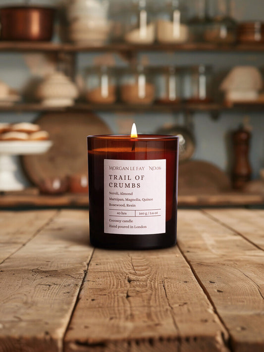 Candle in a glass jar with a label on a wooden surface, with shelves and kitchen items in the background