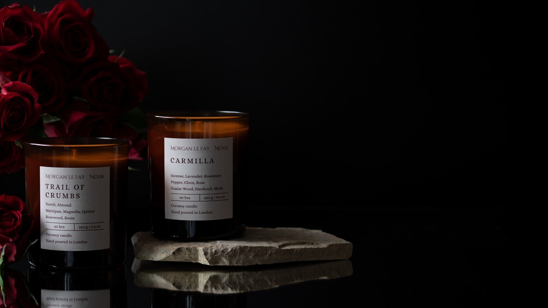 Two candles with labels on a reflective surface against a dark background