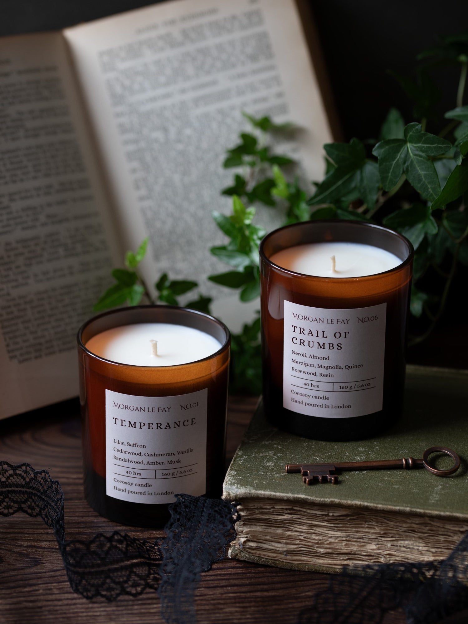 Two candles with labels on a surface with books and a key in the background
